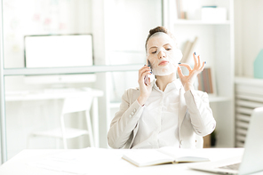 Businesswoman having cotton mask on her face while speaking by smartphone at workplace in office