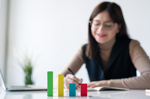 Multi-color cube chart on desk on background of female banker or broker making notes in copybook