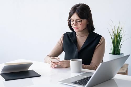 Businesswoman scrolling in smartphone while having drink at break in the middle of working day in office