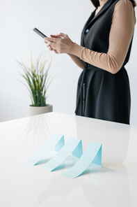 Row of blue paper charts on desk on background of businesswoman scrolling in smartphone in office