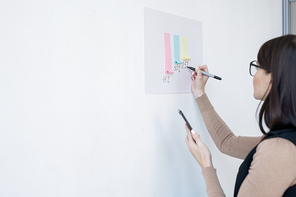 Young female economist making presentation of financial chart while standing in front of whiteboard in office