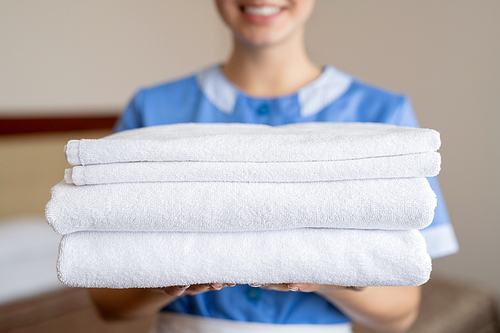 Stack of white clean soft towels held by young smiling housewife or chambermaid inside hotel room