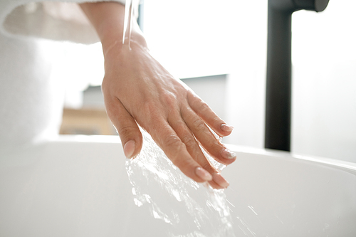Hand of young woman under pure warm water flowing from tap into bathtub before having morning bath