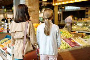 Rear view of young woman and her daughter standing in front of display with fresh fruits inside supermarket