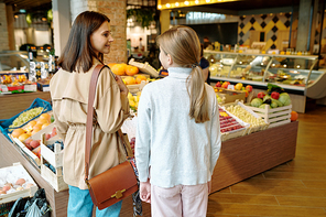 Back view of youthful girl and her mother deciding what to buy in supermarket while standing by fruit display