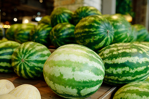 Pile of green large watermelons lying on wooden display inside contemporary supermarket