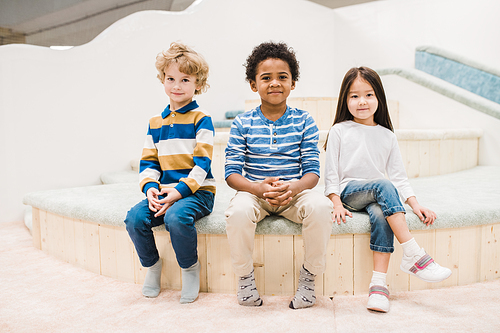 Small intercultural group of cute little kids sitting in front of camera in modern play center for children