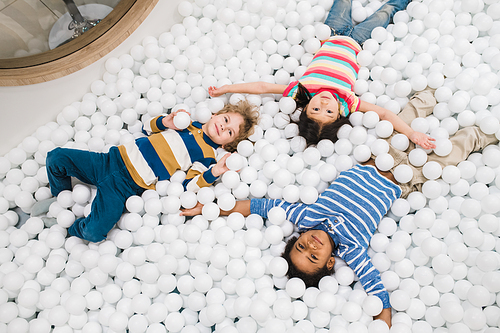Group of cute intercultural little children in casualwear having fun while playing among white balloons on the floor