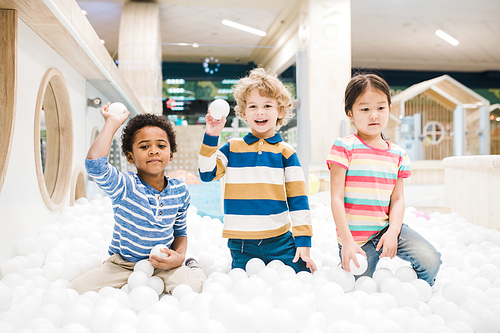 Group of adorable little children in casualwear having fun while playing with white balloons at leisure center