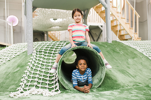 Cute little Asian girl and her friend of African ethnicity having fun on play area in contemporary leisure center