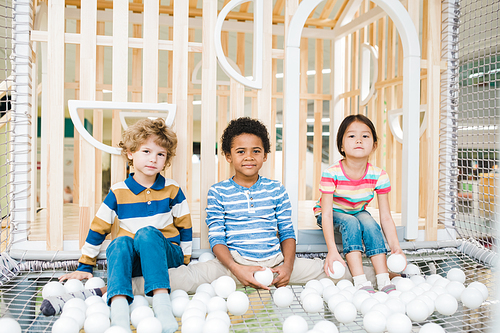 Three cute children of various ethnicities playing with white balloons on playground at leisure center