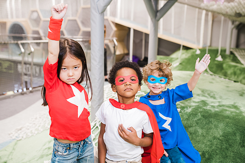 Group of intercultural children in attire of superheroes standing in front of camera during play in kindergarten