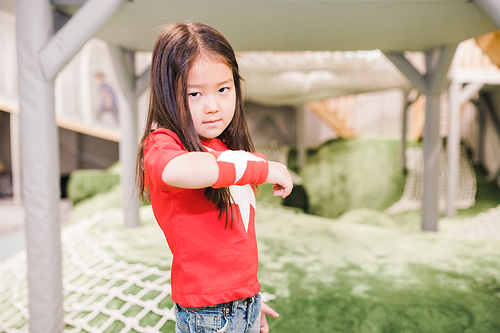 Adorable little girl of Asian ethnicity wearing red t-shirt and handband with white stars playing in kindergarten