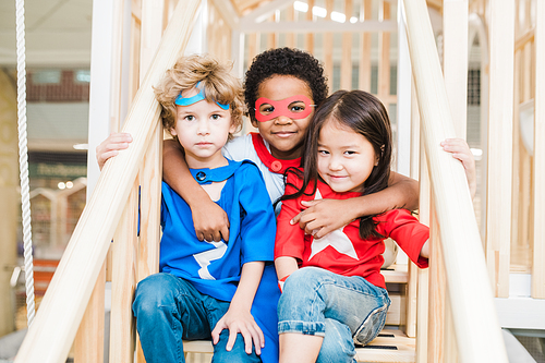 Group of three affectionate little friends of various ethnicities sitting on staircase on play area while spending time together