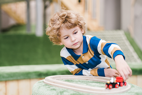 Adorable little boy in casualwear lying on the floor of playground while playing toy trains in kindergarten or leisure center