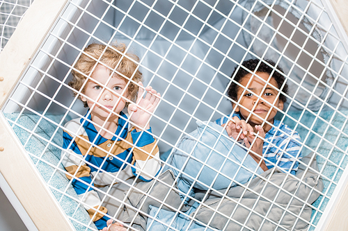 Two cute preschool boys of African and Caucasian ethnicities relaxing on pillows behind bars on play area