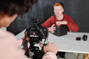 Hands of young operator by camera shooting contemporary male vlogger unpacking box by desk in studio