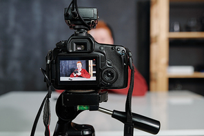 Video camera with young male vlogger or photographer with photocamera on screen during shooting in studio