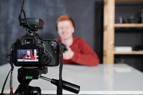 Screen of video camera with young male vlogger or photographer holding photocamera during shooting in studio