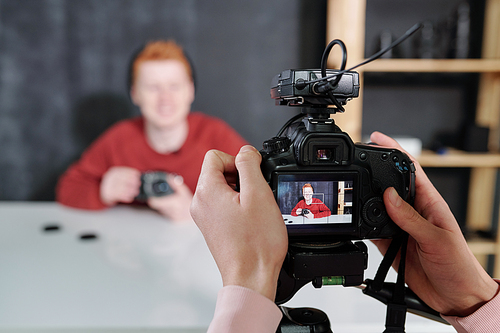 hands of video operator holding camera in front of male Vlog showing new photo equipment while sitting by desk