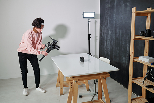 young video Vlog in casualwear shooting new photo equipment while standing by desk in studio