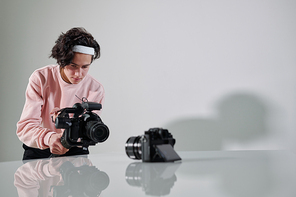 young serious video Vlog standing in front of new photo equipment on desk while shooting it in studio