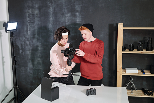 Two male vloggers in casualwear looking at digital screen of camera while discussing recorded video in studio