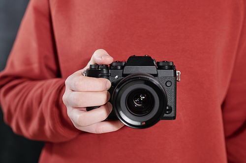 Hands of contemporary male photographer in maroon sweatshirt holding new photocamera in front of himself