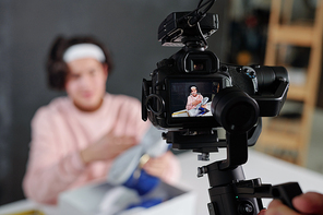 Young vlogger in casualwear showing new sneakers and describing them on display of digital video camera