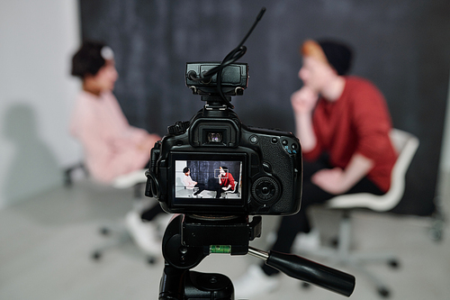 Screen of digital video camera with two vloggers sitting on chairs in front of each other and talking in studio