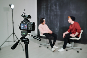 Screen of digital video camera with two vloggers sitting on chairs in front of each other and talking in studio