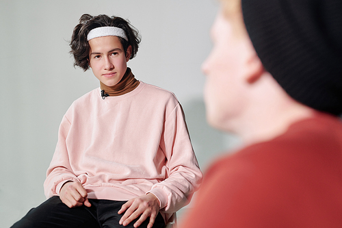 Young serious man in powdery pink pullover and white headband interacting with vlogger sitting in front of him