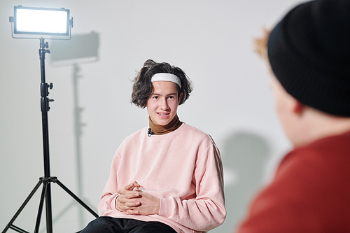 Handsome young man in powdery pink pullover and white headband communicating with vlogger in front of him