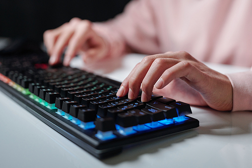 Hands of teenager over keys of computer keyboard typing while sitting by desk and doing homework