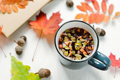 Mug with hot black herbal tea on table with acorns and mixture of red maple and rown leaves