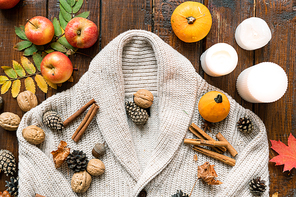 Composition of burning candles, ripe apples and pumpkins, cinnamon sticks, walnuts, acorns, leaves and firtree cones on warm sweater
