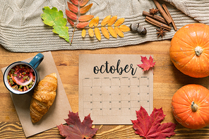 October calendar among fresh pastry with tea, ripe pumpkins, leaves and spices on wooden table