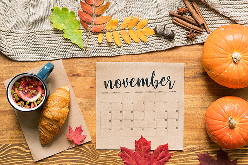 November calendar with hot drink and croissant, ripe pumpkins, autumn leaves and spices near by