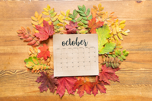 October calendar sheet on wooden table among red, green and yellow autumn leaves