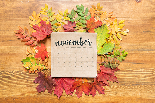 Top view of November calendar sheet surrounded by autumn leaves of various colors