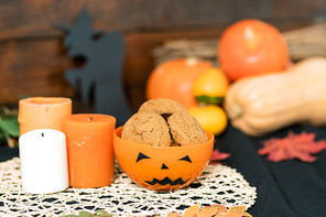 Orange halloween plastic bowl with cookies and three candles on white knitted napkin with pumpkins on background