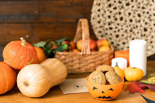 group of ripe pumpkins, orange  plastic bowl with cookies on background of candles and basket with apples