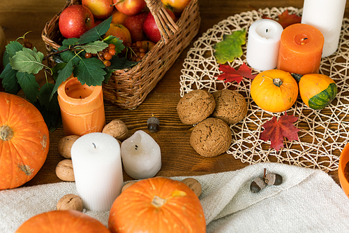 Autumn composition of ripe pumpkins, candles, oat cookies, leaves and basket with apples on wooden table