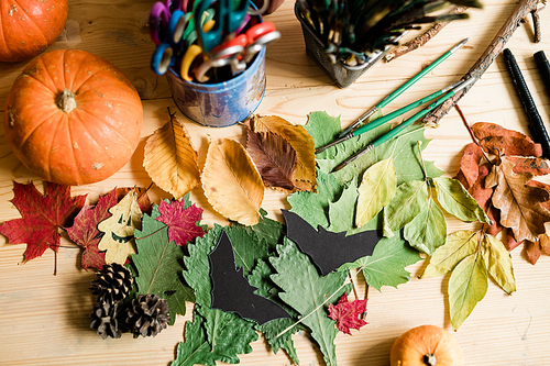 Autumn background with dry colorful leaves, ripe pumpkins, pinecones, paintbrushes and crayons on wooden table