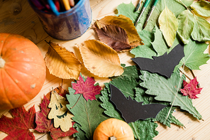 Autumn background with dry colorful leaves, ripe pumpkins, black paper bats and paintbrushes on wooden table