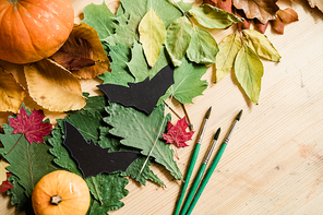 Composition of dry colorful leaves, gourds, handmade black paper bats and paintbrushes on wooden table