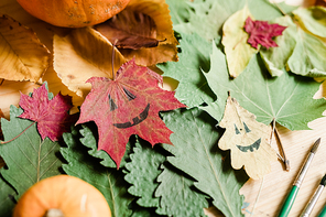 Background or overview of dry autumn foliage, halloween faces on leaves and paintbrushes