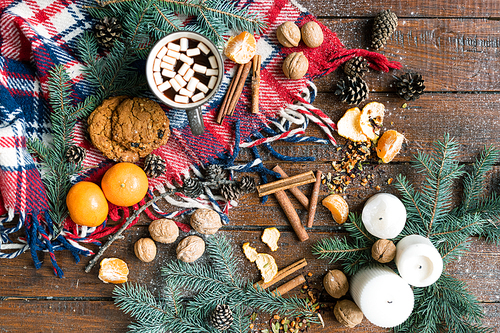 Christmas background consisting of conifer, walnuts, candles, firtree cones, hot drink, cookies, mandarines, cinnamon and scarf on wooden table