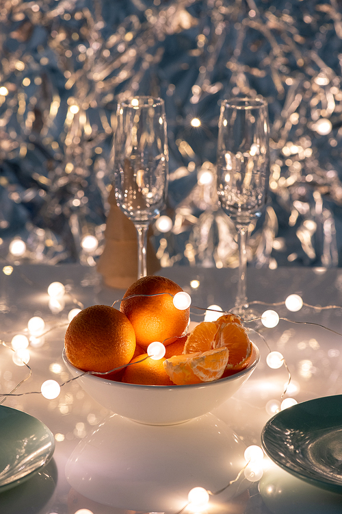 White porcelain bowl of oranges with garlands and two flutes on table served for celebration of new year