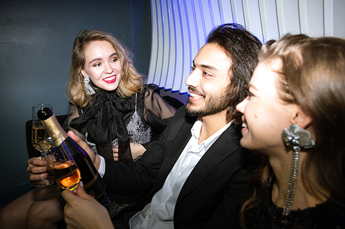 Happy glamorous girls and young man with champagne sitting on couch in night club and enjoying party